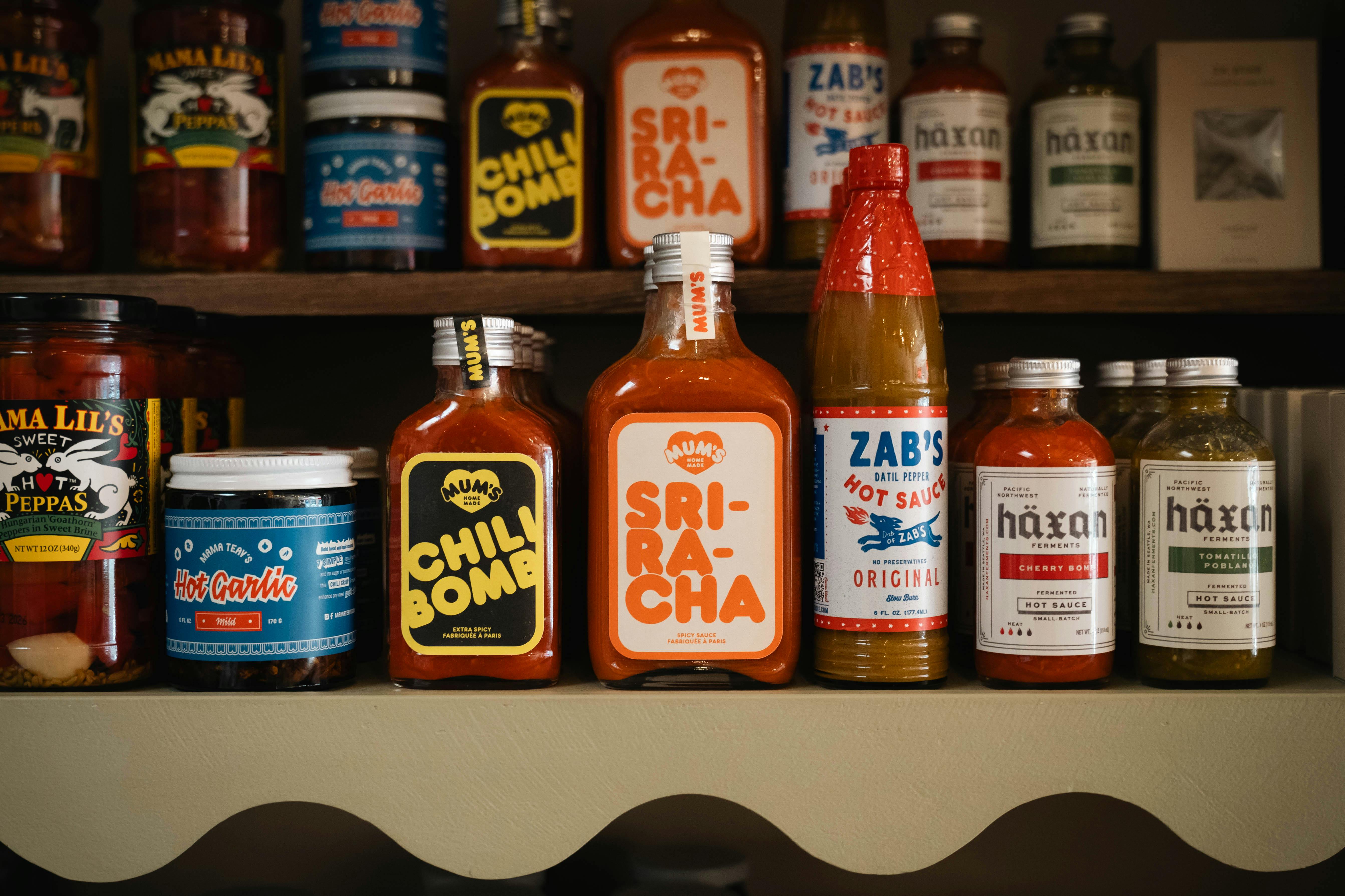 A variety of hot sauce bottles displayed on a shelf, featuring different brands and spice levels